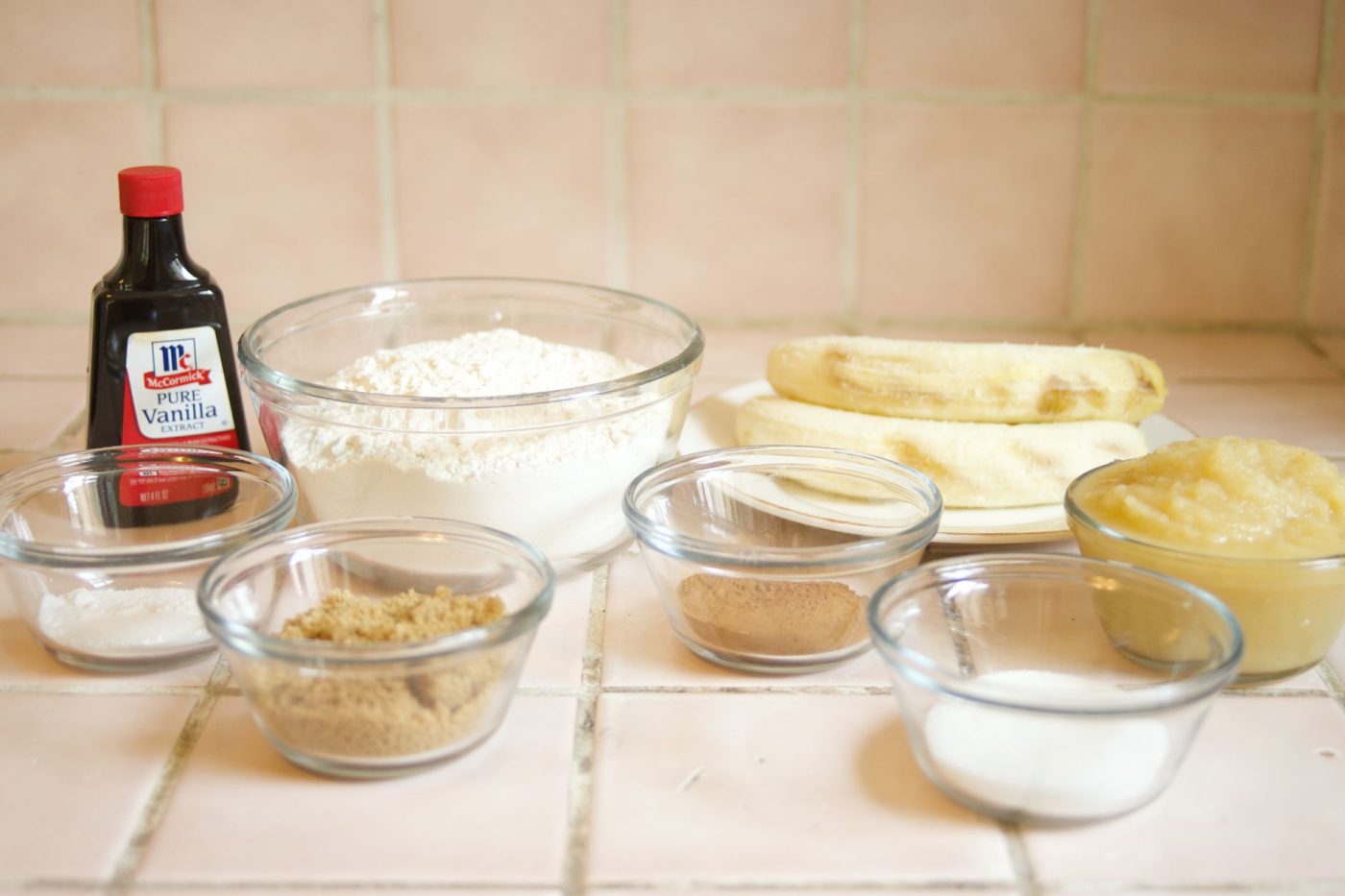 Assorted ingredients for gluten free banana nut bread arranged on a kitchen counter, including ripe bananas, walnuts, eg