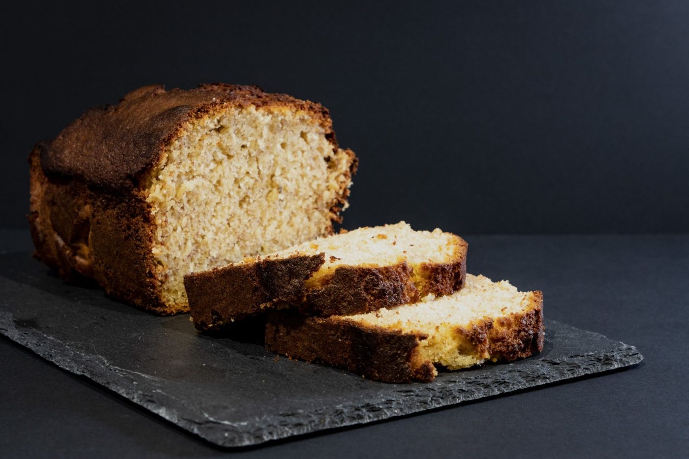 A hand slicing into a freshly baked gluten free banana nut bread loaf, revealing a moist, tender crumb with visible waln