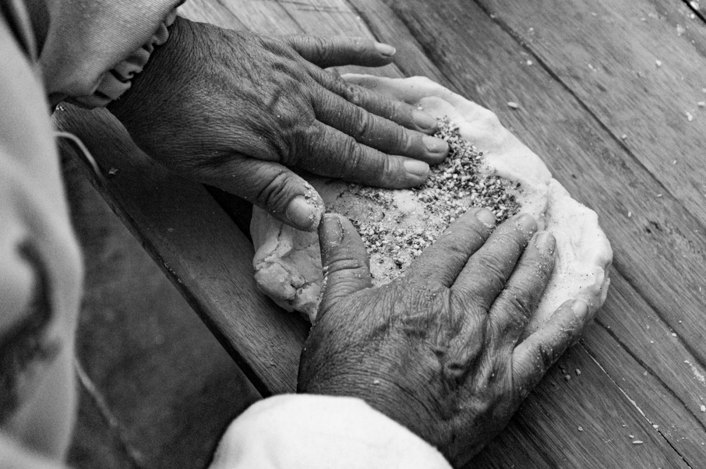 A person sprinkling seeds into bread dough inside a bread machine pan.