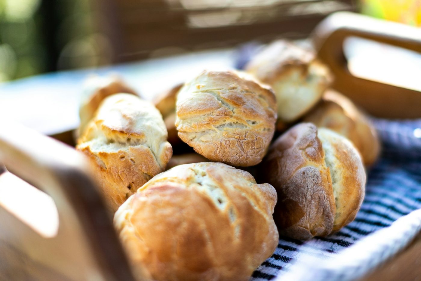 A wire basket lined with a cloth holding several soft gluten free dinner rolls on a kitchen counter.