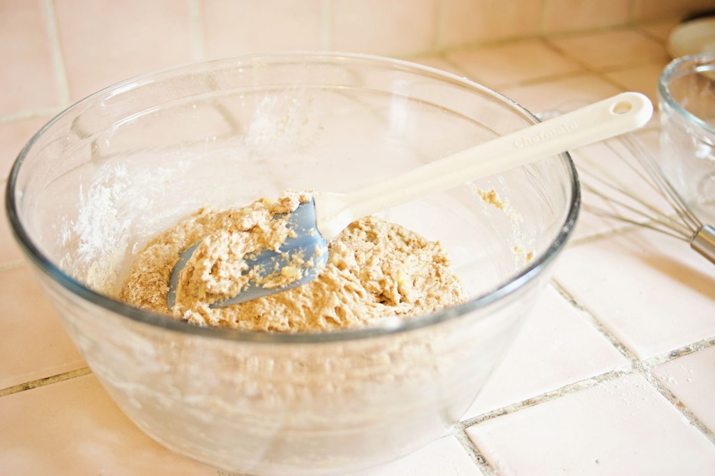A mixing bowl filled with gluten free flour, yogurt, and other ingredients for making naan bread on a kitchen counter.
