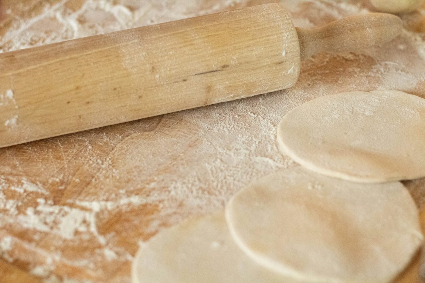 A person's hands rolling out gluten free naan dough on a floured wooden board in a home kitchen.