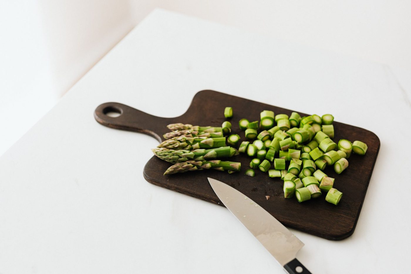 A wooden cutting board with chopped broccoli, bell peppers, and zucchini next to a knife in a home kitchen.