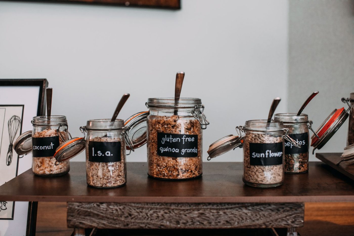 Open kitchen shelves with labeled glass jars of gluten-free pasta, rice, and quinoa in a bright home kitchen.
